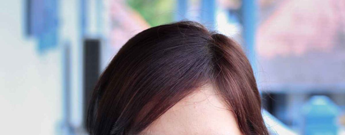 Een jonge vrouw gezien vanaf de neus blikt de camera in, zij heeft sluit donkerbruin haar in een scheiding uit het midden